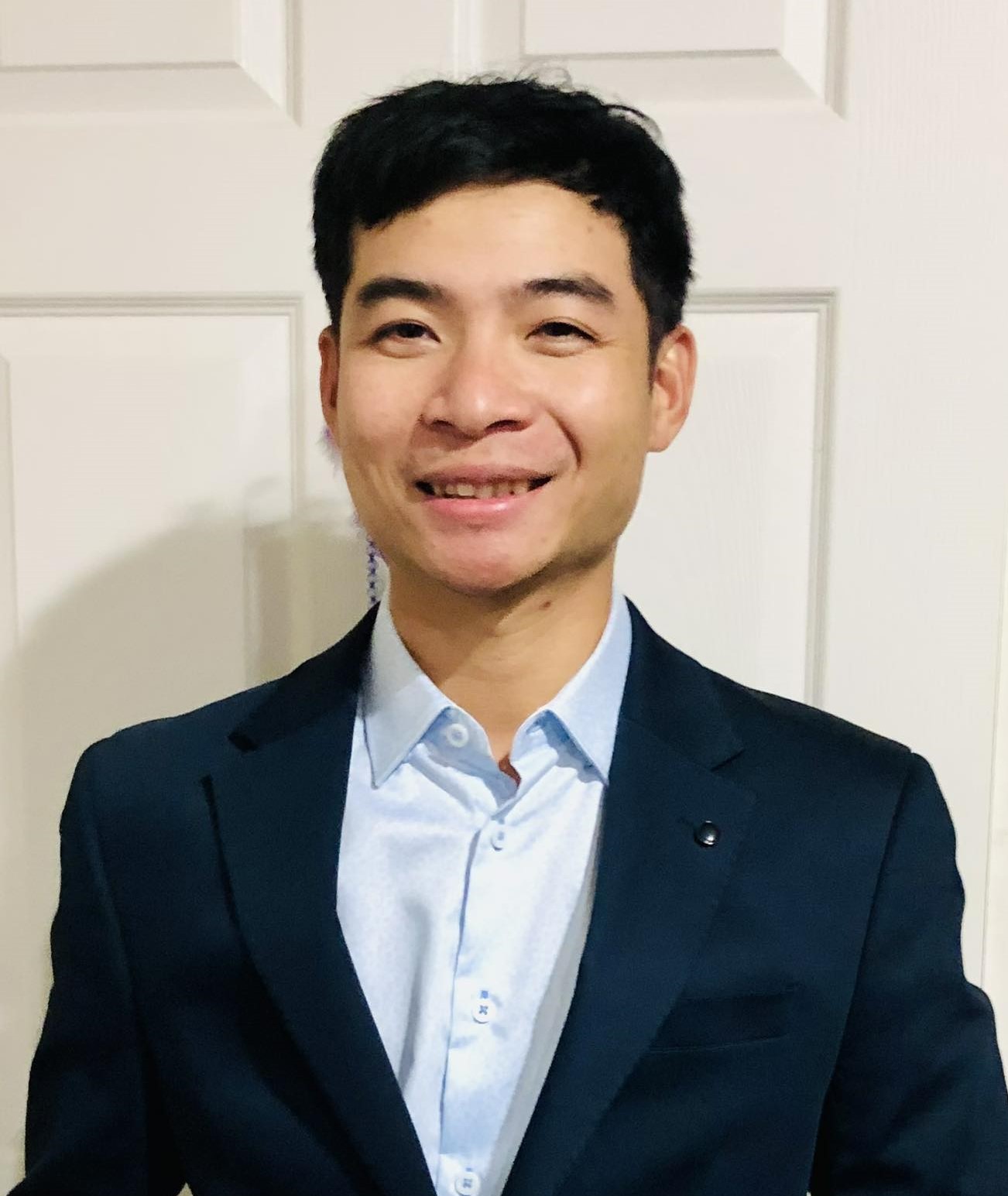 Young man in suit shirt and jacket with black hair smiling at the camera.