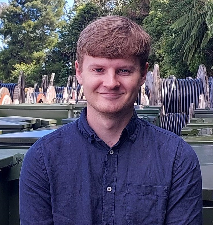 A young man with light brown hair and blue shirt smiling at the camera.