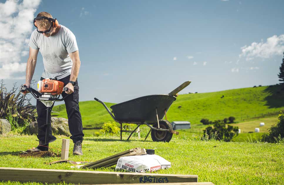 Person digging using a post hole borer on farm