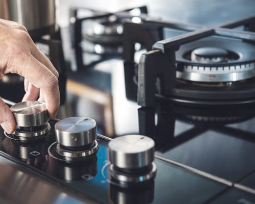 A hand turning on a gas hob