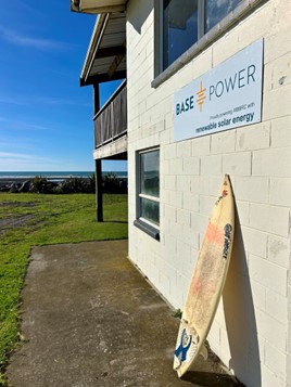 A surf board leaning against a building, below a sign saying Base Power