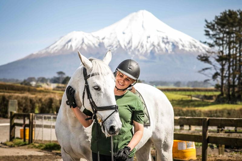 Woman standing next to white horse with mountain in back ground