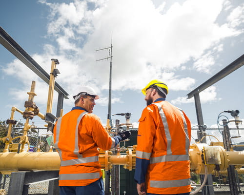 Two people in PPE standing in front of Powerco gas infrastructure